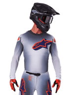 2025 Supertech Lipan Jersey, Motocross Racing Jersey, Gray with Orange and Navy Blue accents, long-sleeve performance top with perforated ventilation details, worn with black helmet and red gloves, sleek racing design
