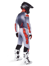 Motocross rider from a back-side profile wearing 2025 Supertech Lipan Jersey and matching pants in Gray and Orange Fluo, featuring bold orange Alpinestars branding on the sleeves and legs, paired with a black helmet and white boots, coordinated pro-level outfit for off-road racing