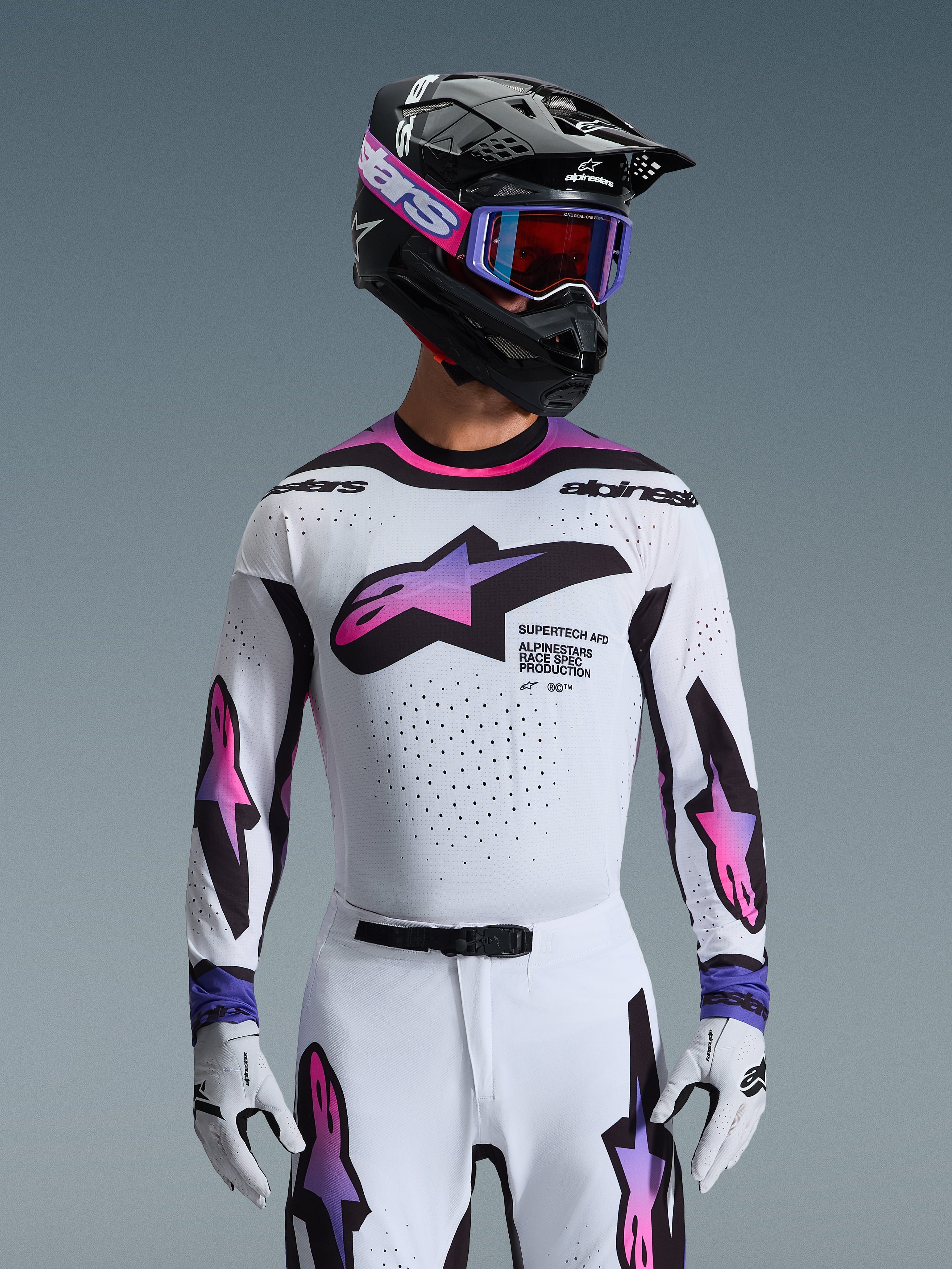 Alpinestars 2026 Supertech AFD Vista Gear Set, professional motocross racing gear, white jersey and pants with pink and purple gradient graphics, black helmet with purple goggles and white gloves, athletic race fit for off-road performance.