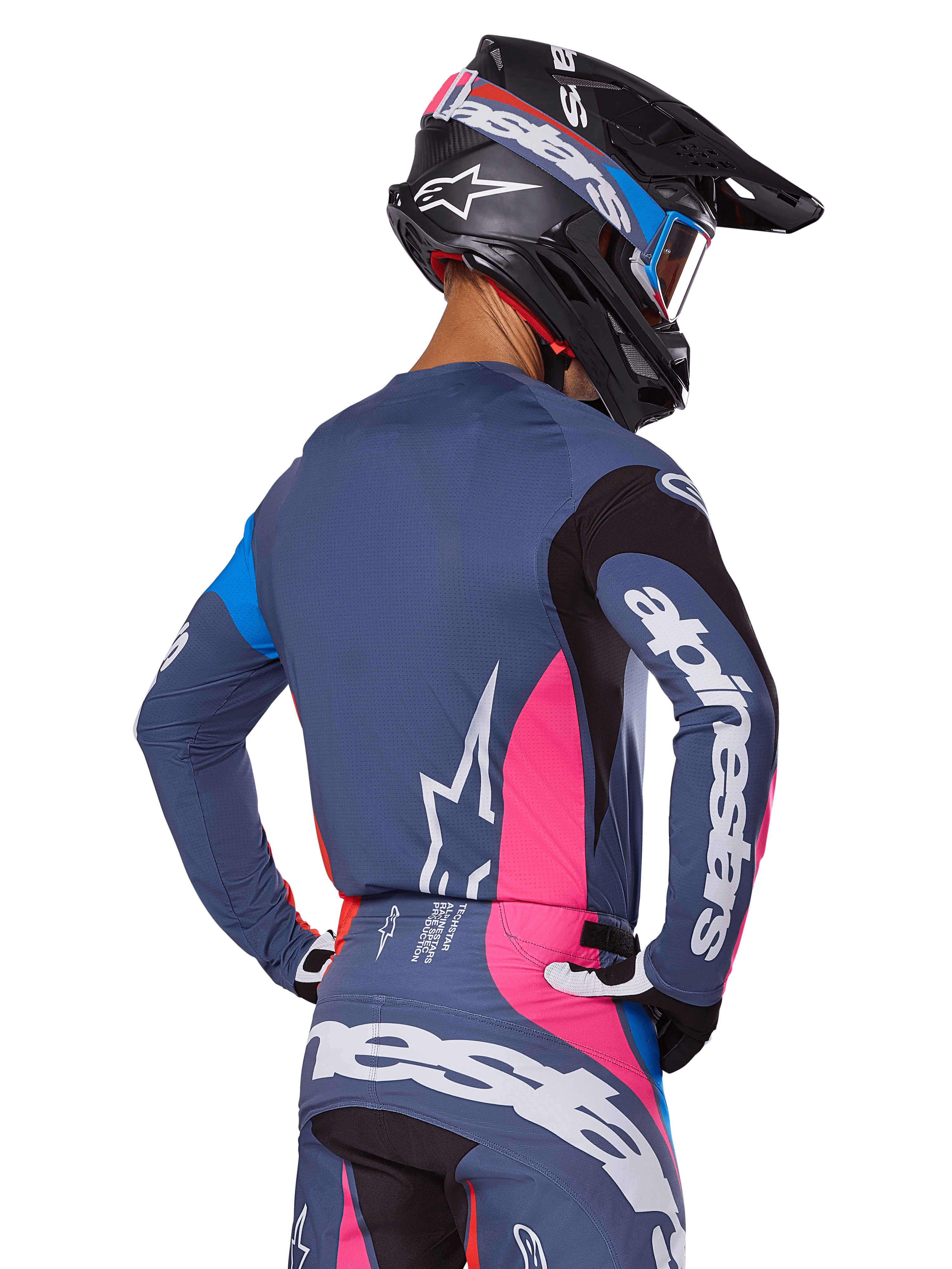 Motocross rider viewed from behind wearing the Alpinestars 2025 Techstar Dreem gear set in Gray, featuring a blue-gray jersey and pants with pink and black panels, white Alpinestars logos on the sleeves and back, and a matching black helmet with blue and pink graphics.