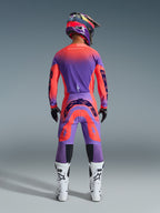 Motocross rider from behind wearing the 2026 Supertech Scenz Gear Set in Hot Coral Purple, vibrant jersey and pants with gradient transition, featuring Alpinestars logos, matching helmet, white and black boots, and black gloves, professional gear for elite off-road racing.