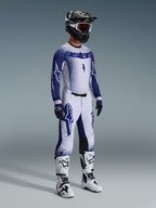 Motocross rider wearing complete professional racing gear, 2026 Supertech Scenz Jersey in light gray and dark blue, matching motocross pants with star graphics, black helmet with red goggles, white and black performance boots, coordinated blue and white gloves for off-road racing