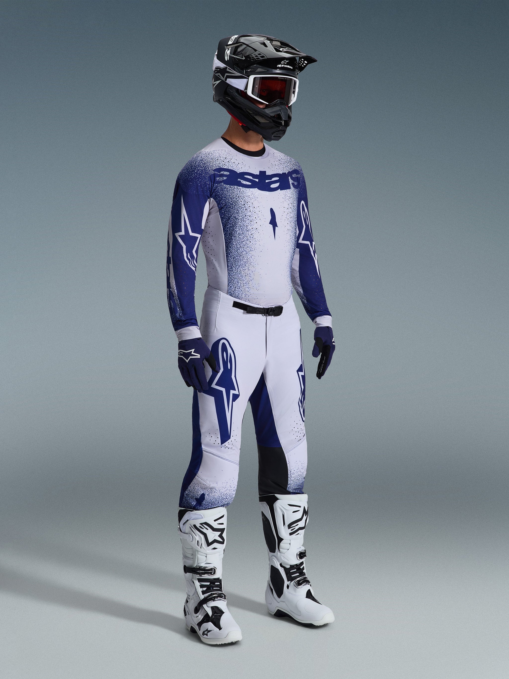 Motocross rider wearing complete professional racing gear, 2026 Supertech Scenz Jersey in light gray and dark blue, matching motocross pants with star graphics, black helmet with red goggles, white and black performance boots, coordinated blue and white gloves for off-road racing