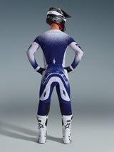 Motocross rider from behind wearing the Alpinestars 2026 Supertech Scenz Jersey, Light Gray and Dark Blue with a stippled gradient design, matching motocross pants, white racing boots, and black helmet, complete off-road racing outfit.