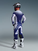 Rear view of a motocross rider wearing the Alpinestars 2026 Supertech Scenz Jersey in Light Gray and Dark Blue, featuring a speckled gradient design, coordinated with matching pants and white motocross boots, professional athletic racing gear.