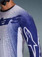 Alpinestars 2026 Supertech Scenz Jersey, Light Gray and Dark Blue, close-up of shoulder and chest showing laser-cut perforations, white Astars logo on blue sleeve, speckled graphic design, professional motocross racing gear.