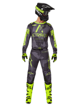 Motocross rider wearing complete racing gear, Alpinestars 2025 Racer Hollow Jersey and matching pants in Dark Camo Yellow Fluo, featuring bold fluorescent yellow graphics on a dark grey camouflage background, paired with matching gloves, bright yellow fluo boots, and a black helmet.