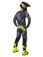 Rear view of a motocross rider wearing the 2025 Racer Hollow Gear Set in Dark Camo Yellow Fluo, featuring a gray camo jersey with yellow fluo accents, matching motocross pants with bold branding on the seat, bright yellow fluo boots, and a black helmet with yellow goggles.
