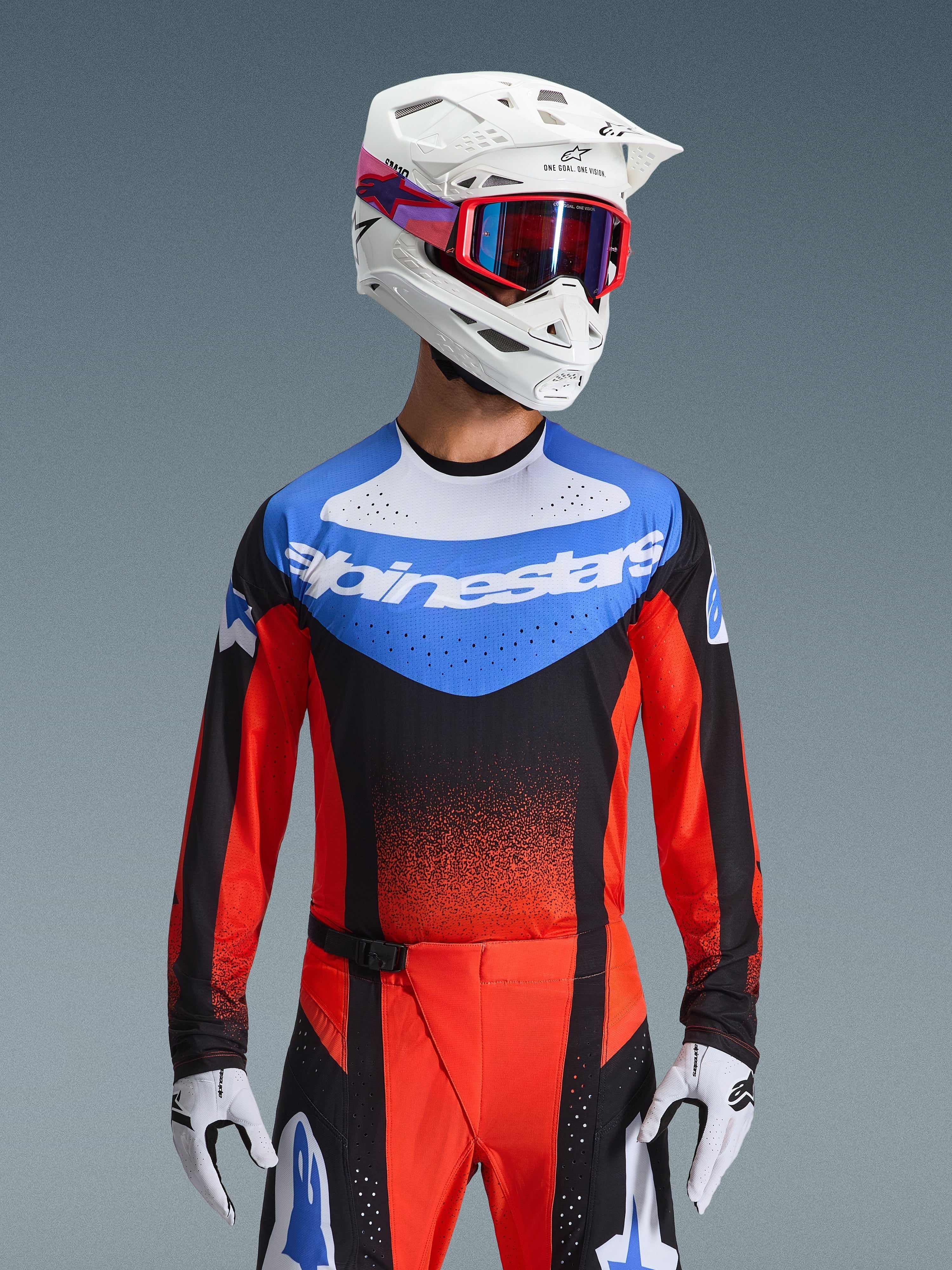 Alpinestars 2026 Techstar Knif Jersey, Motocross Jersey, Orange Black and UCLA Blue, featuring a blue chest panel with white Alpinestars logo and orange-red sleeves, worn with a white helmet, red goggles, and white gloves, professional off-road racing gear