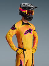 Alpinestars 2026 Techstar Nomur Jersey, Motocross Jersey, Orange Yellow and Pink, worn by a rider with a matching black helmet and goggles, featuring a large pink star logo on the chest, black accents, and laser-cut ventilation details.
