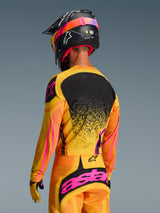 Alpinestars 2026 Techstar Nomur Jersey in Orange Yellow Pink, rear view of a motocross rider wearing full gear including matching pants and a black helmet, vibrant design with yellow and pink accents and black back panel, athletic race-fit for off-road performance