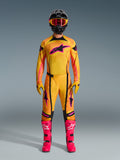 2026 Techstar Nomur Gear Set, complete motocross racing apparel worn by a rider, yellow and orange gradient jersey with pink star logo, matching pants and gloves, bright pink boots and black helmet, professional MX kit on a gray background