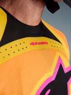 Close-up of the Alpinestars 2026 Techstar Nomur Jersey, Orange Yellow and Pink colorway, showing laser-cut ventilation perforations, seamless black collar, and pink branding details on perforated stretch fabric.