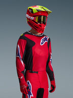Motocross rider wearing the Alpinestars 2026 Fluid Grid Jersey in Red Black and Purple, coordinated with matching motocross pants, a red helmet with neon yellow accents, gold goggles, and red gloves, complete off-road racing outfit.