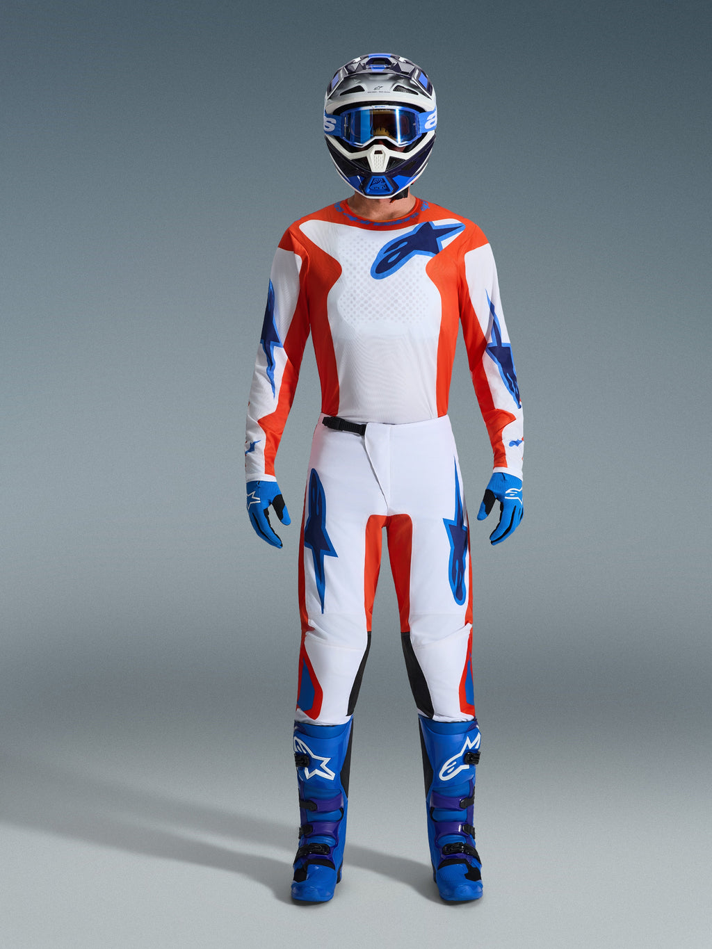 Alpinestars 2026 Fluid Grid Gear Set, Motocross rider wearing full gear, white jersey and pants with orange and UCLA blue accents, matching blue and white helmet with blue goggles, blue gloves, and blue motocross boots, coordinated off-road racing outfit