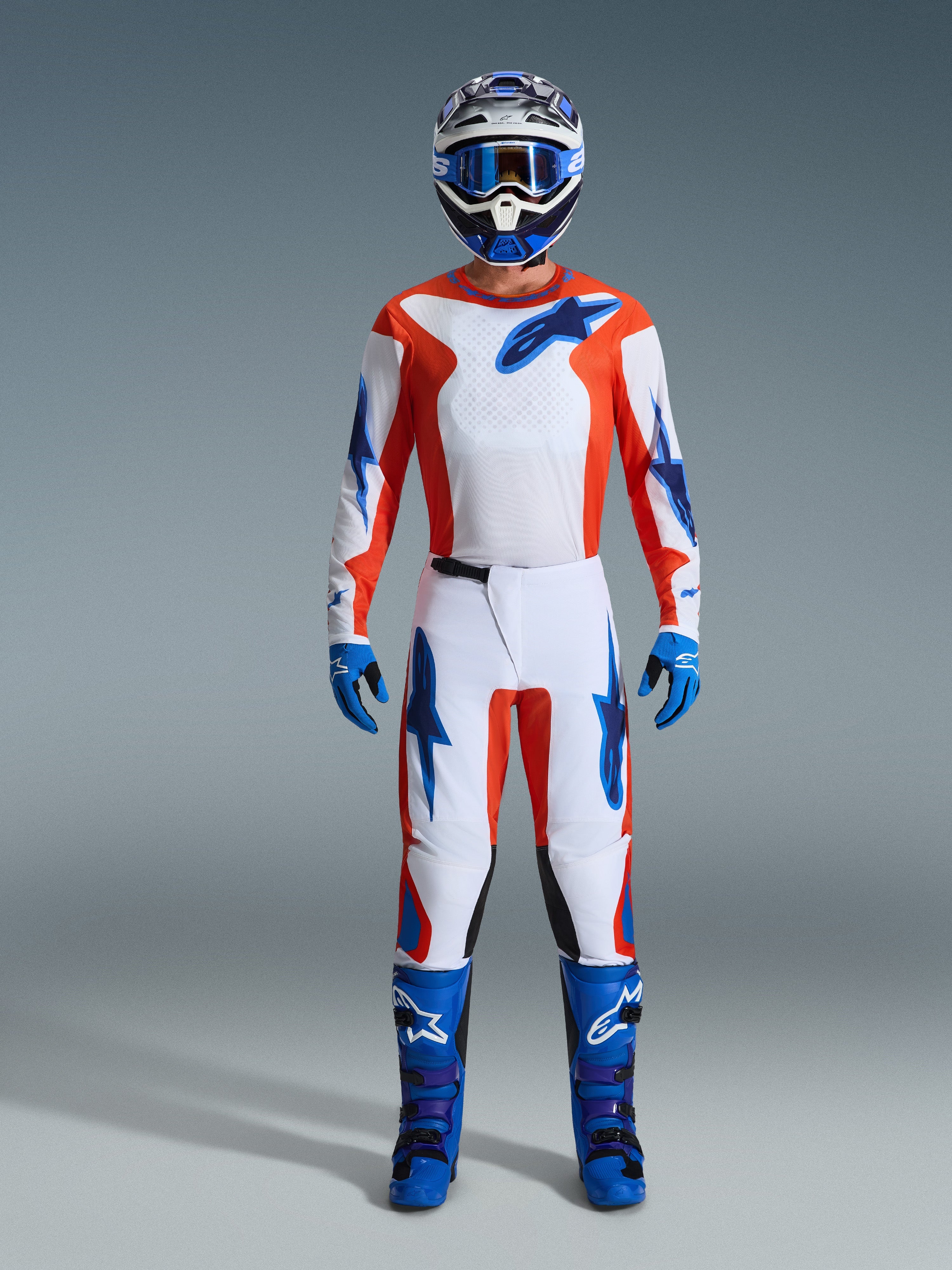Alpinestars 2026 Fluid Grid Gear Set, Motocross rider wearing full gear, white jersey and pants with orange and UCLA blue accents, matching blue and white helmet with blue goggles, blue gloves, and blue motocross boots, coordinated off-road racing outfit
