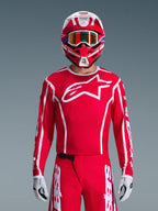 Motocross rider wearing complete Alpinestars 2026 Fluid Apex Gear Set, red jersey with large white star logo on the chest, matching red pants with white branding, red and white helmet with iridescent goggles, white and black gloves, coordinated red and white outfit for off-road racing