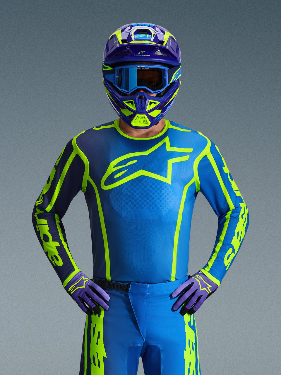 Motocross rider wearing the Alpinestars 2026 Fluid Apex Jersey in Blue Yellow Fluo, featuring a vibrant blue base with fluorescent yellow graphics and a large chest logo, coordinated with a matching helmet and gloves, designed for off-road and motocross racing