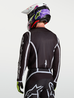 Alpinestars Fluid Apex V2 Jersey, Black and Silver motocross racing top on model viewed from the back, featuring moisture-wicking polyfabric and ergonomic cut.