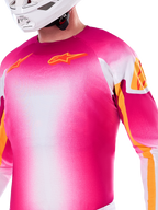 Alpinestars Limited Edition Supertech AFD MIG Jersey, Motocross Jersey in Pink Fluo and White gradient, featuring orange Astars logos and sleeve accents, worn by a rider with a white helmet, athletic racing fit.