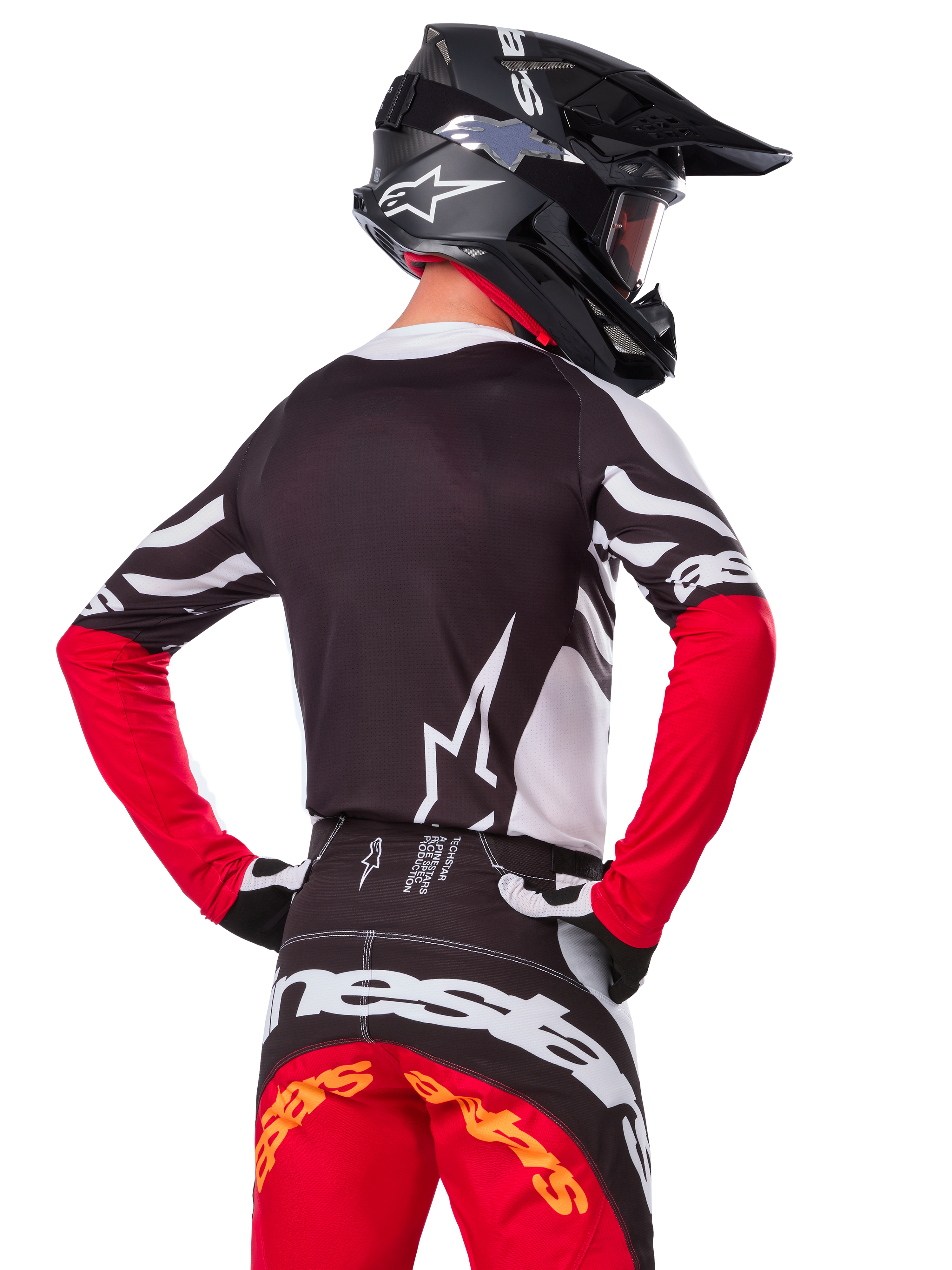 Motocross rider from the back wearing the Alpinestars Limited Edition Techstar Deep Jersey, Black White and High Red, with matching racing pants and a black helmet, athletic fit for off-road performance