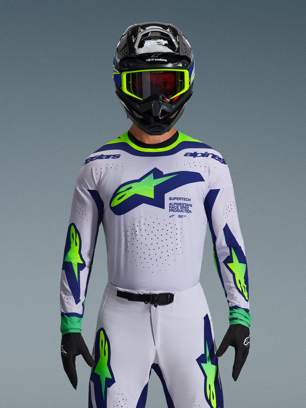 Alpinestars 2026 Supertech Vista Gear Set, Motocross Jersey and Pants, White with Blue and Neon Green graphics, worn with a black helmet and neon goggles, featuring laser-cut ventilation and athletic race fit for professional racing.
