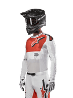 Alpinestars 2024 Supertech Ward Jersey, Motocross Jersey, White and Hot Orange, featuring a red chest panel with white star logo, long sleeves with laser-cut perforations, worn with a black helmet and white gloves, athletic race fit motocross gear