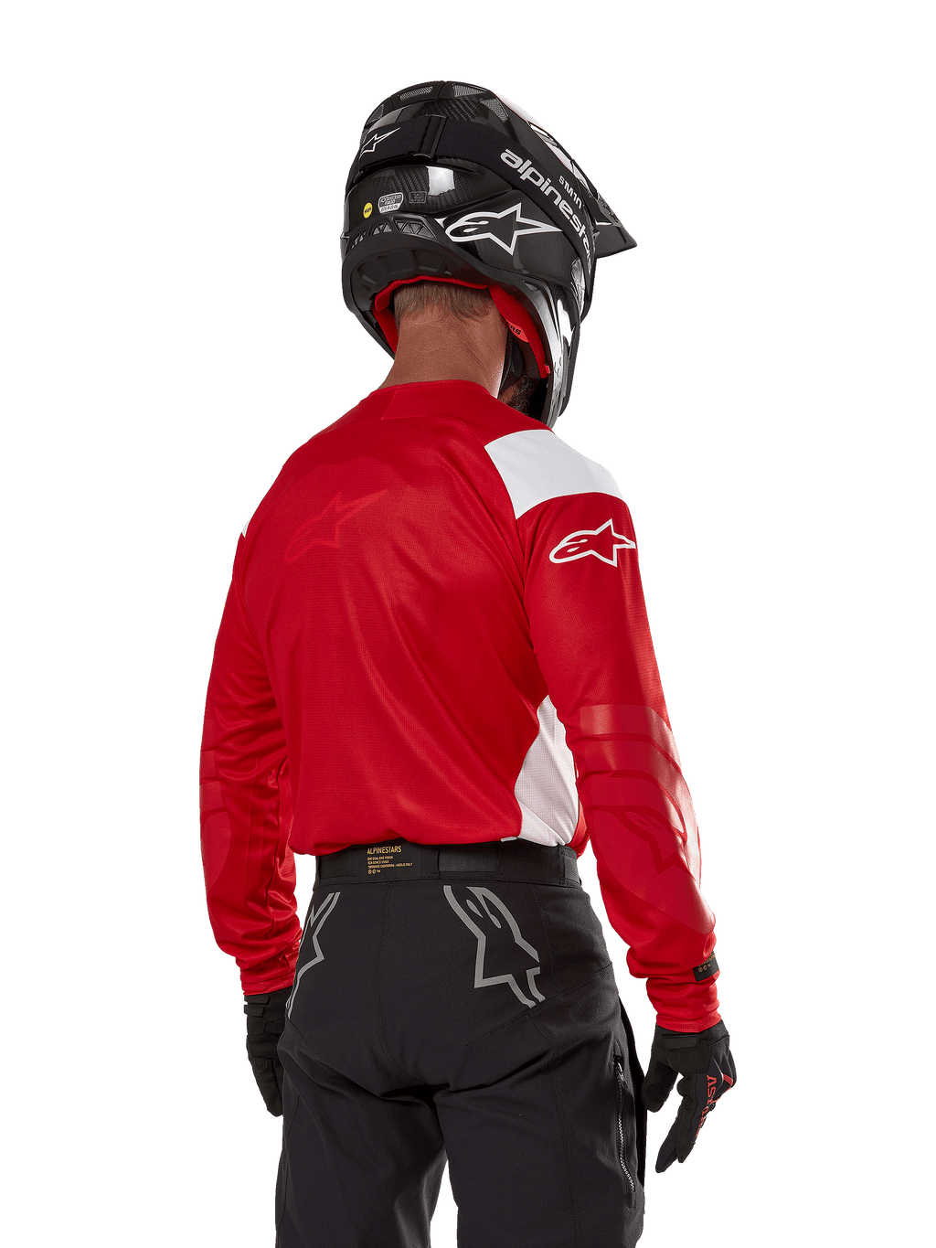 Motocross rider seen from the back wearing the Alpinestars Techdura Jersey in Bright Red with white panels, paired with black off-road pants, a black helmet, and black gloves, coordinated gear for enduro and motocross riding.