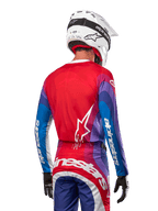 Motocross rider from behind wearing Alpinestars 2024 Techstar Pneuma Jersey in Blue Mars Red White, featuring a red back with white star logo, blue and purple sleeves with white branding, coordinated with matching pants and a white helmet for off-road racing.