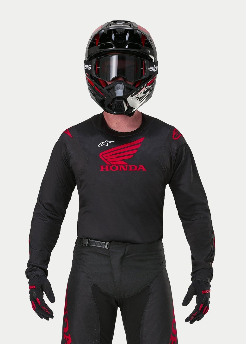 Motocross rider wearing the Alpinestars Honda Racer Iconic Jersey in Black and Red, featuring a large red Honda wing logo on the chest and white Astar logo, paired with a matching black helmet, goggles, and gloves for a complete off-road racing kit