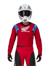 Motocross rider wearing the Alpinestars Honda Racer Iconic Jersey, Red with blue shoulder panels and white Honda logo, paired with matching red and black pants and a white motocross helmet, professional off-road racing gear