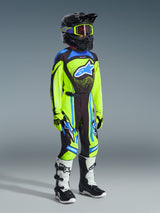 Youth motocross rider wearing complete racing gear, 2026 Youth Supertech Nomur Jersey in Yellow Fluo and Dark Navy, matching pants with blue accents, black helmet with fluorescent yellow goggles, white and black boots, coordinated outfit for off-road racing