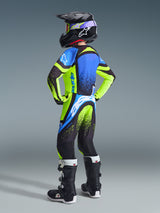 Alpinestars 2026 Youth Supertech Nomur Jersey and pants, youth motocross rider seen from behind wearing full racing gear, vibrant yellow fluo and dark navy with UCLA blue accents, matching black helmet and boots, coordinated pro-level off-road outfit