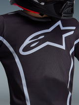 Alpinestars 2026 Youth Fluid Apex Jersey, Close-up of chest design, Black and Gray, featuring a prominent light gray star logo and athletic piping, worn with a black helmet, performance motocross gear for youth riders