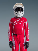 Alpinestars 2026 Youth Fluid Apex Jersey, Red and White, worn with matching motocross pants, white helmet with black goggles, and black gloves, featuring a large white logo and athletic fit for youth off-road racing.