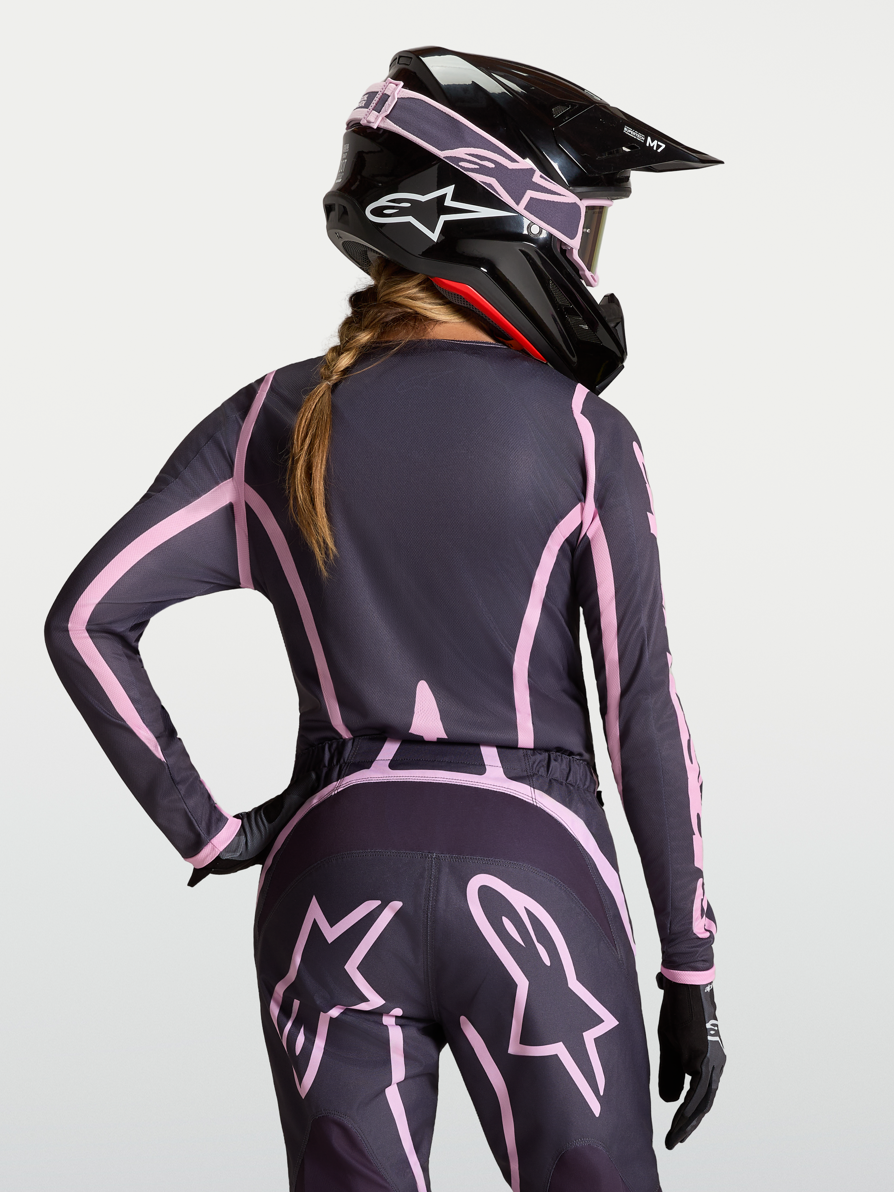 Alpinestars Stella Fluid Apex V2 Jersey, women's motocross gear in Graystone and Old Pink, moisture-wicking polyfabric riding shirt with extended rear coverage, shown on-model with a matching helmet.