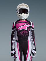 Female motocross rider wearing the 2026 Alpinestars Stella Techstar Nomur Jersey, Black White and Fuchsia design with a large pink logo on the chest, matching racing pants and gloves, white helmet with goggles, complete coordinated gear for off-road competition.