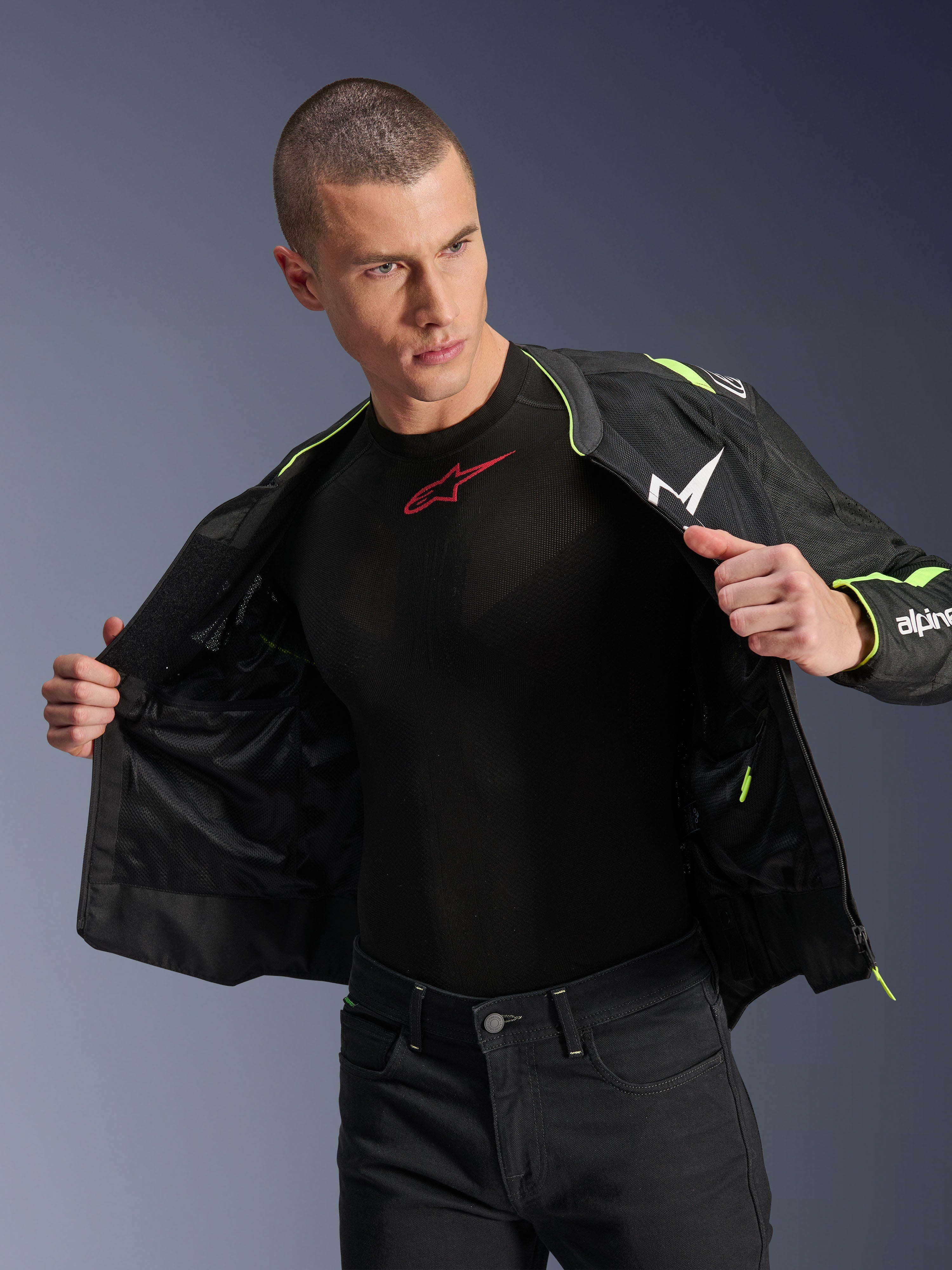 Male model wearing the Alpinestars T-Sps Air V2 Jacket in Black and Yellow Fluo, shown open to highlight the internal mesh construction and pocketing, paired with a black Alpinestars base layer and black pants, urban motorcycle riding gear style