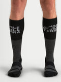 Alpinestars AT-8 Merino Socks, men's all-terra adventure motorcycle socks in tar gray and black, over-the-calf thermal merino-blend performance apparel worn on model showing ribbed upper calf and reinforced cushioning zones.