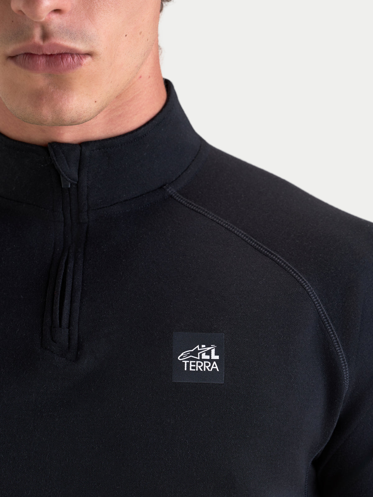 Alpinestars AT-8 Merino Top Layer, men's adventure touring motorcycle base layer in black, close-up view showing the technical 250g dual-layer Merino construction, quarter-zip collar, raglan sleeves, flatlock seams, and All Terra chest branding worn by a model.