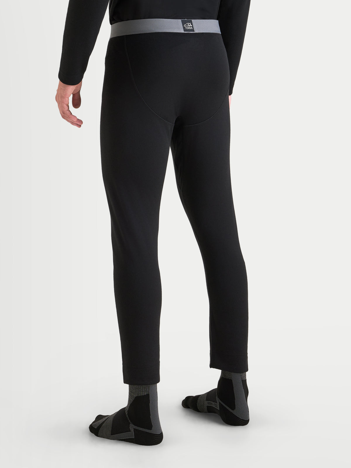 Alpinestars AT-8 Merino Bottom Tech Layer, men's motorcycle thermal base layer in black, rear view on a model showing seamless construction, elasticated waistband, and moisture-wicking Merino wool fabric.