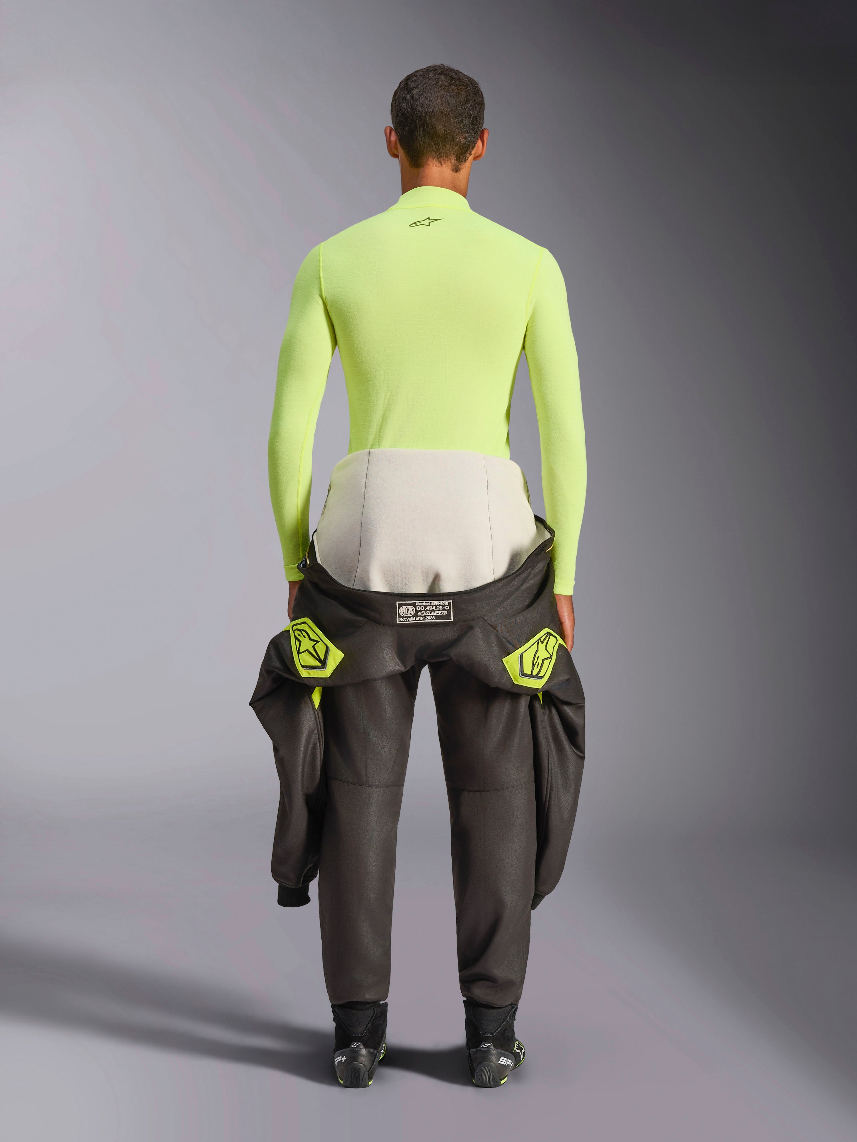 Alpinestars ZX Evo V3 Top, Long Sleeve Base Layer, Yellow Fluo, back view of a driver with a racing suit tied around the waist, vibrant neon yellow flame-resistant top featuring a small black logo on the neck and a slim athletic fit