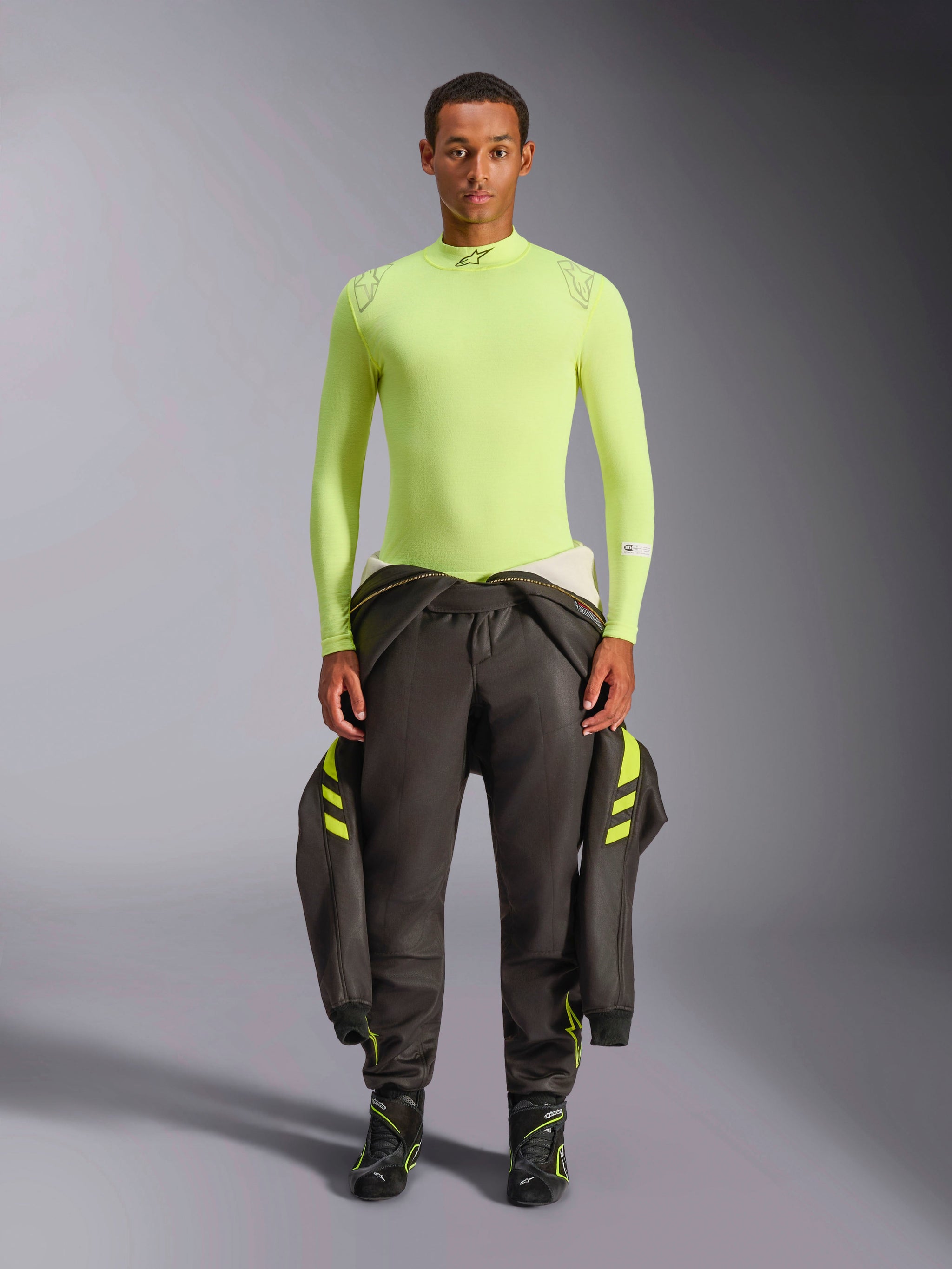 Alpinestars ZX Evo V3 Top - Long Sleeve, Yellow Fluo, worn by a model with dark racing pants and boots, featuring a mock neck and athletic fit, fire-resistant base layer for professional auto racing