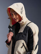 Alpinestars Molly Air Jacket in Black Almond, worn by a female model with the hood up, featuring cream and black color-blocking, a vibrant orange mesh lining, and technical urban design elements including a star logo and zip details.