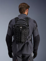 Alpinestars AT-15 Back Pack, adventure motorcycle backpack, Black Deep Gray, worn by a person over a gray technical riding jacket, showing the back view with 'ALL TERRA' branding, ergonomic design with reinforced textured panels and secure straps.