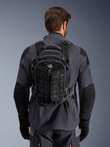 Alpinestars AT-15 Back Pack in Black Deep Gray, technical adventure backpack worn by a rider from the back, featuring textured front panels and 'ALL TERRA' branding, paired with a gray and black motorcycle riding jacket.