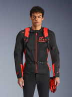 Man wearing Alpinestars MM93 AMP3 Backpack, Red Fluo and Black, featuring adjustable shoulder straps and buckled chest strap, styled with a matching MM93 motorcycle jacket and gloves, technical gear from the Marc Marquez collection