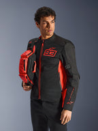 Alpinestars MM93 Waist Bag, Red Fluo and Black, held by a model wearing a matching black and red motorcycle jacket, featuring multiple zippered compartments and Marc Marquez branding, practical gear for sport riding