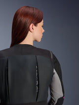 Alpinestars Women Stella Tech-Air® 3 V2 System, black motorcycle airbag vest, close-up back view on a model with red hair, featuring textured textile panels and grey mesh accents, slim-fit autonomous protection for urban and road riding