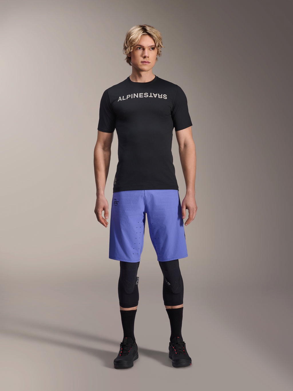 Alpinestars A-Aria Lite Short in Baja Blue, Men's MTB Shorts, worn with a black short-sleeve jersey and protective knee guards, featuring laser perforations for ventilation, mountain bike performance gear